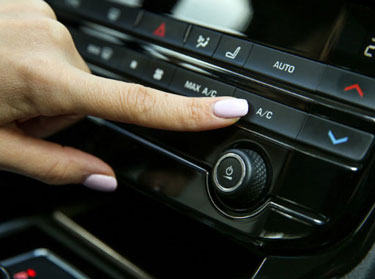 Driver pressing the A/C button on a car's climate control panel