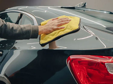 Hand polishing a dark car's paint with a microfiber towel