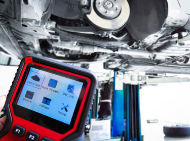Handheld OBD-II diagnostic scanner in front of a car on a lift