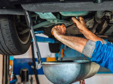 Mechanic draining used oil into a pan under a lifted car